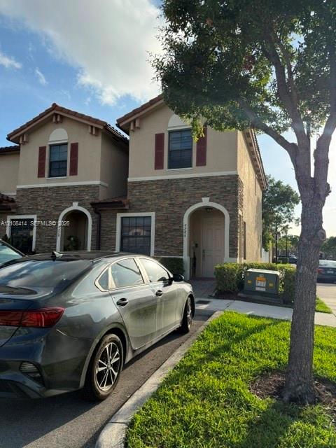 Two-story exterior featuring multi-textured facade with stone veneer and stucco, arched entryway, and dark-toned shutters