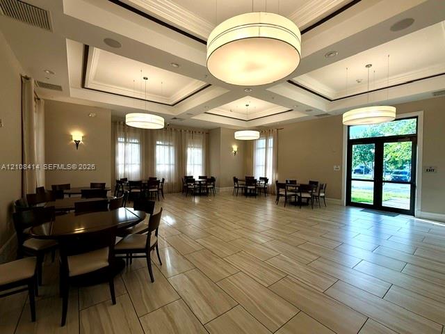 Expansive multipurpose room featuring high coffered ceilings, large drum-style pendant lighting, tile flooring, and floor-to-ceiling windows