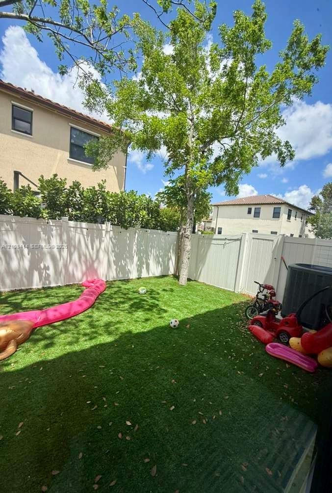 Backyard featuring synthetic turf, privacy fencing, and a mature tree