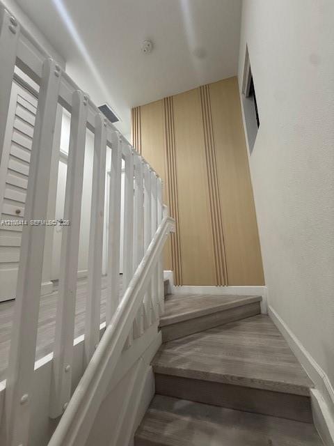 Staircase featuring wood-finish treads, a white balustrade, and a decorative light wood panel accent wall with vertical slat detailing