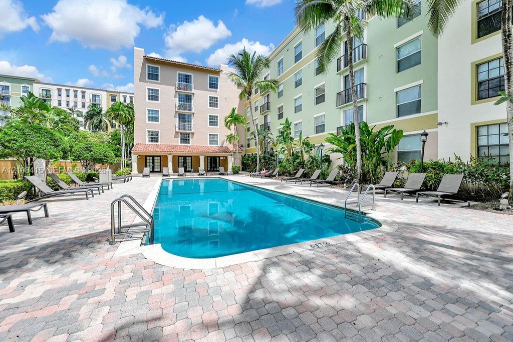 In-ground pool with metal handrails, surround finished in stone pavers, and landscaped grounds featuring mature palms
