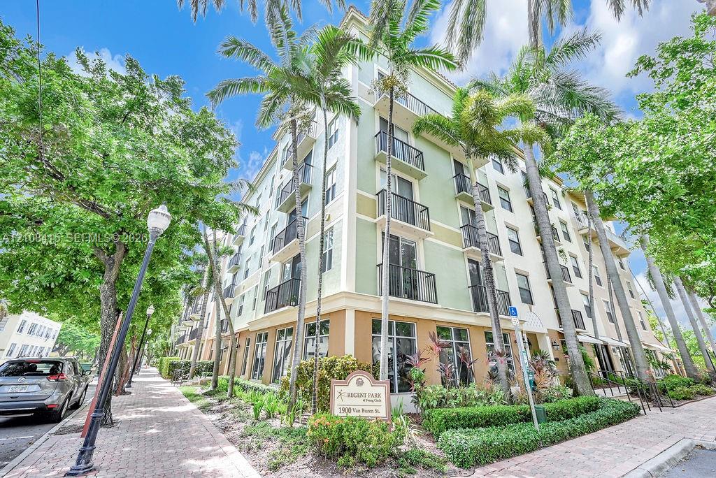 Multi-story building exterior featuring a stucco facade, metal balcony railings, floor-to-ceiling windows, and surrounding palm tree landscaping Multi-story building exterior featuring a stucco facade, metal balcony railings, floor-to-ceiling windows, and surrounding palm tree landscaping