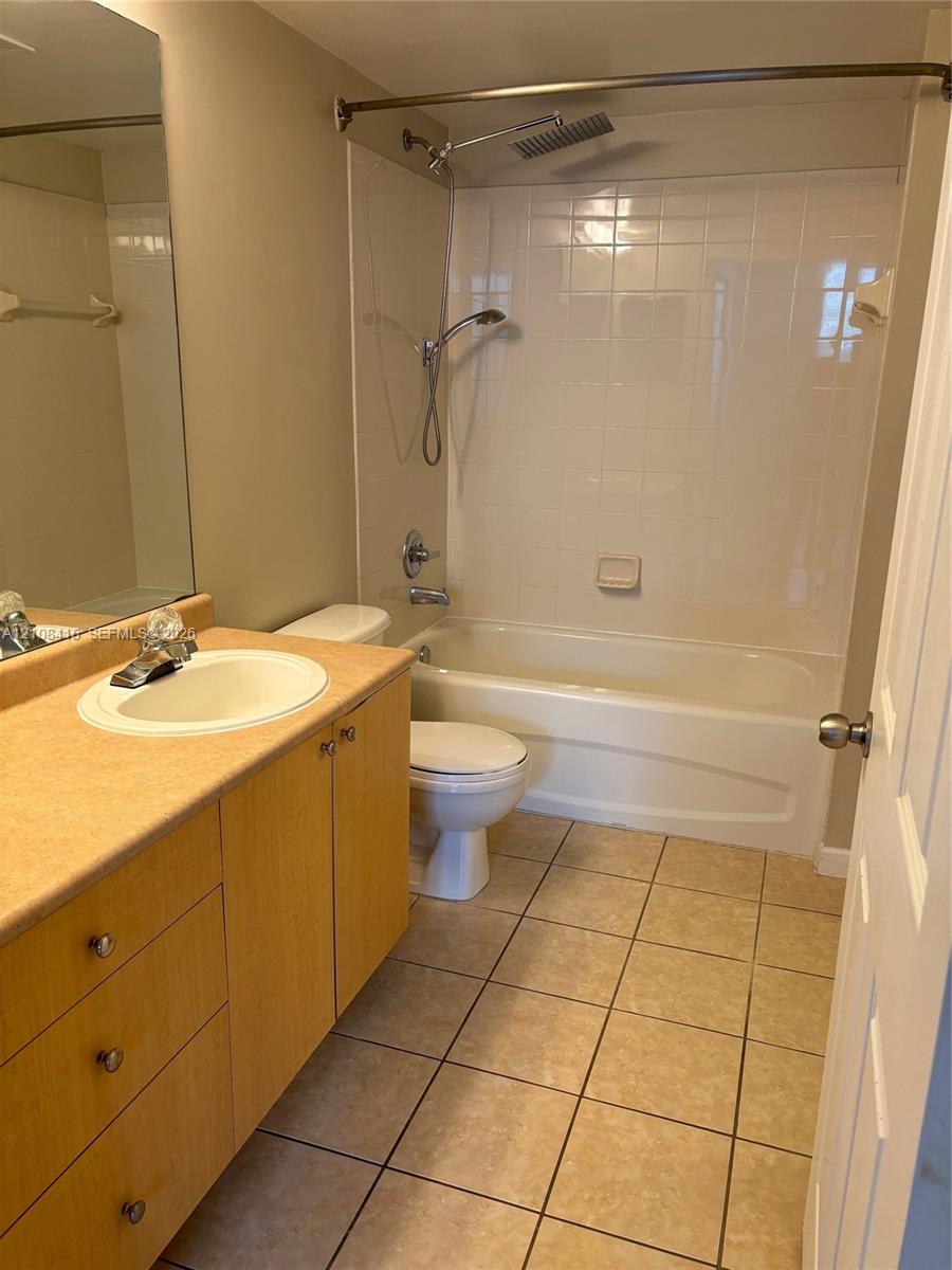Bathroom featuring wood-finish cabinetry, a drop-in sink, ceramic tile flooring, a shower-tub combination with tile surround, and a handheld showerhead