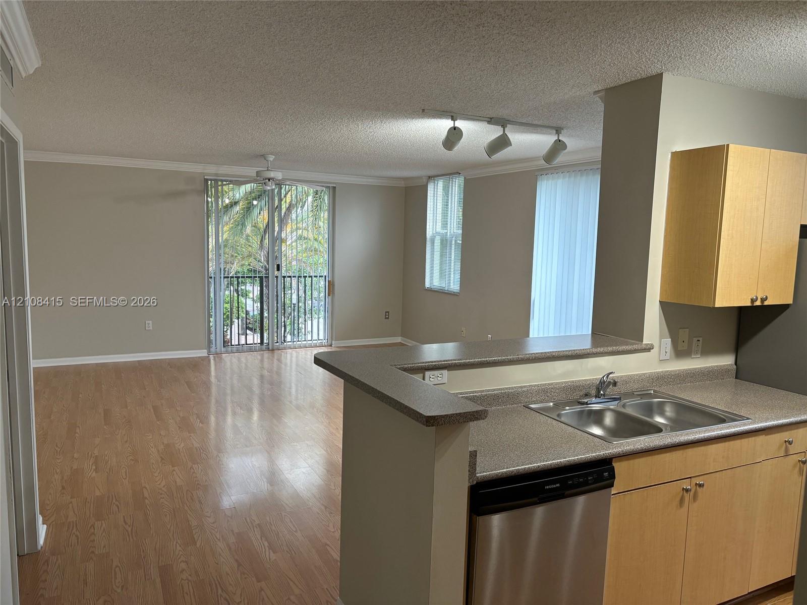 Open-concept interior featuring wood-finish flooring, a breakfast bar, stainless steel dishwasher, light-finish cabinetry, and a sliding glass door