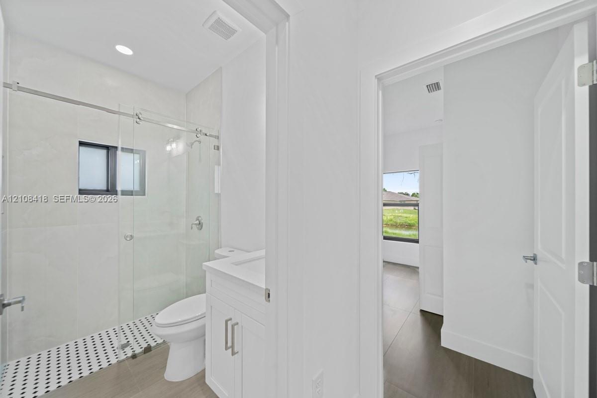 Bathroom featuring a glass-enclosed shower with a black and white tiled floor, vanity cabinet with a stone-surface countertop, recessed lighting, and wood-finish flooring
