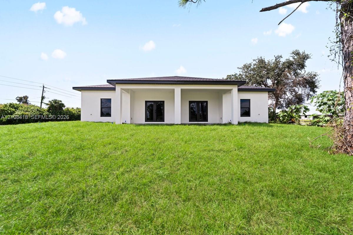 Exterior elevation featuring a light-colored stucco facade, dark-toned hip roof, recessed covered patio, and dark-framed windows and doors