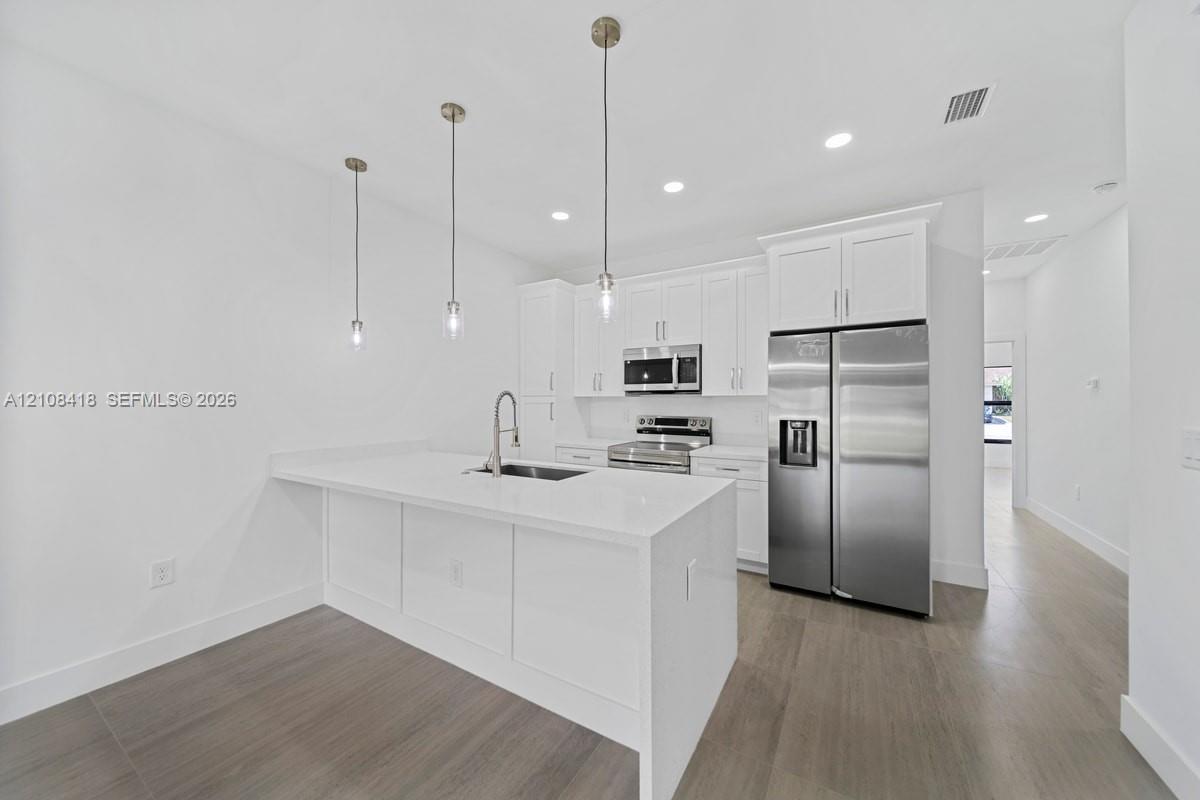 Kitchen featuring white cabinetry, quartz countertops, a central island with a stainless steel sink, stainless steel appliances, and wood-finish flooring
