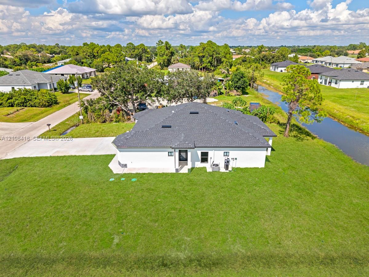 Single-story residence featuring a shingled roof, white exterior finish, concrete driveway, and expansive lawn area situated along a canal