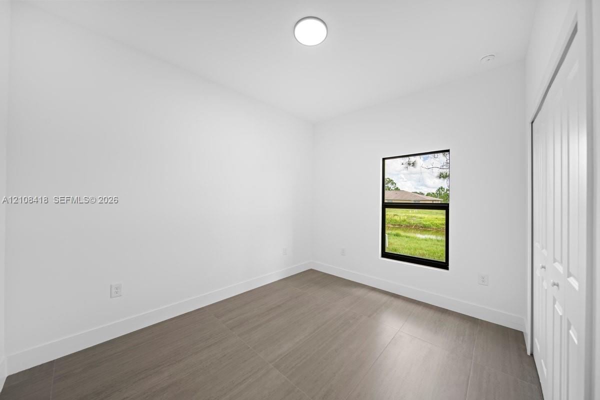 Neutral interior featuring wood-finish flooring, a flush-mount ceiling light, a single window with a black frame, and a bi-fold closet door