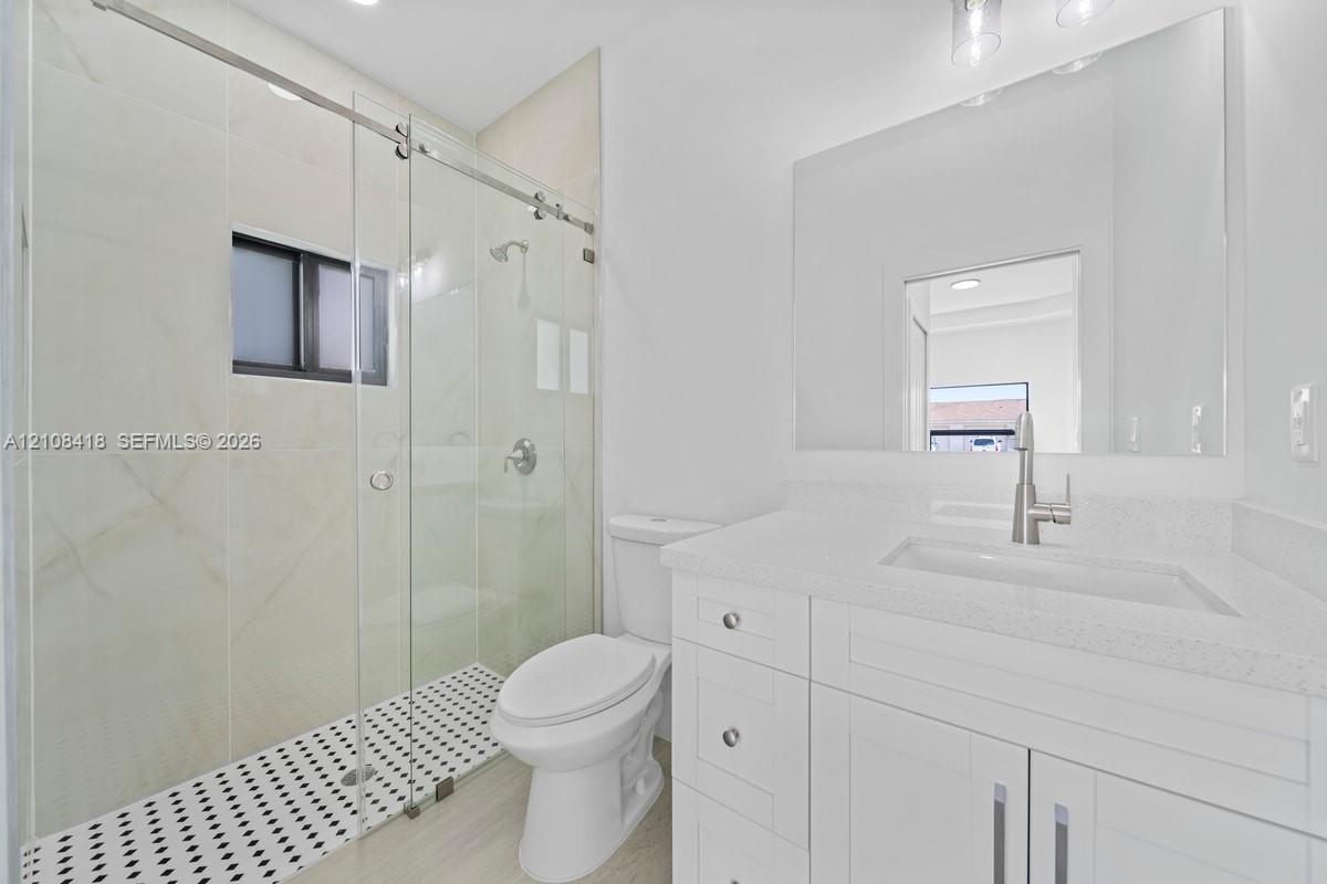 Walk-in shower featuring a glass enclosure, large-format tile surround, and black-and-white mosaic floor tiling, complemented by a white vanity with a quartz countertop and a rectangular undermount sink