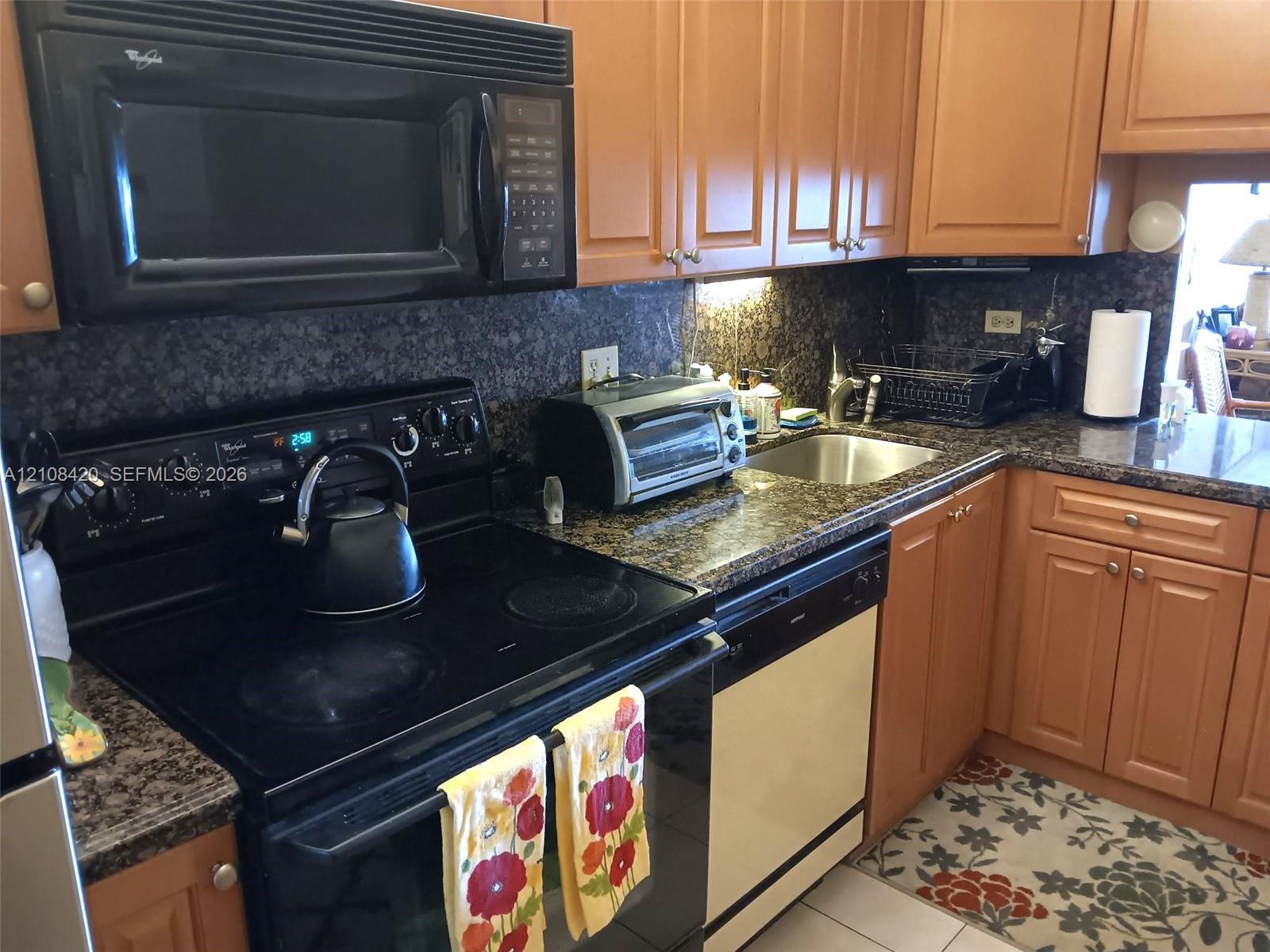 Kitchen featuring medium-tone wood cabinetry, dark stone countertops, an integrated over-the-range microwave, a smooth-top electric range, and a stainless steel undermount sink Kitchen featuring medium-tone wood cabinetry, dark stone countertops, an integrated over-the-range microwave, a smooth-top electric range, and a stainless steel undermount sink