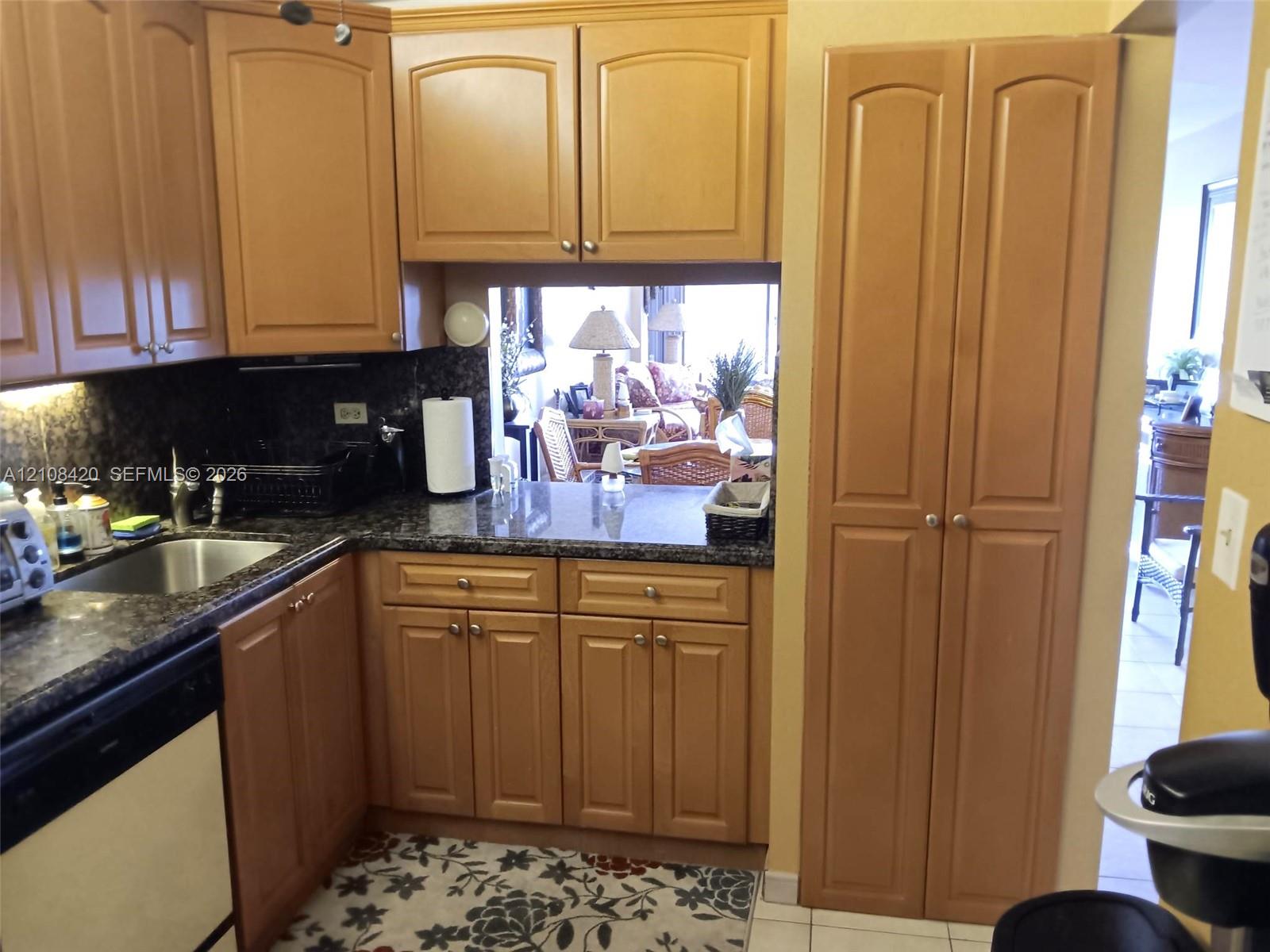 Kitchen featuring wood cabinetry, stone countertops, stainless steel undermount sink, built-in dishwasher, and a floor-to-ceiling pantry cabinet Kitchen featuring wood cabinetry, stone countertops, stainless steel undermount sink, built-in dishwasher, and a floor-to-ceiling pantry cabinet