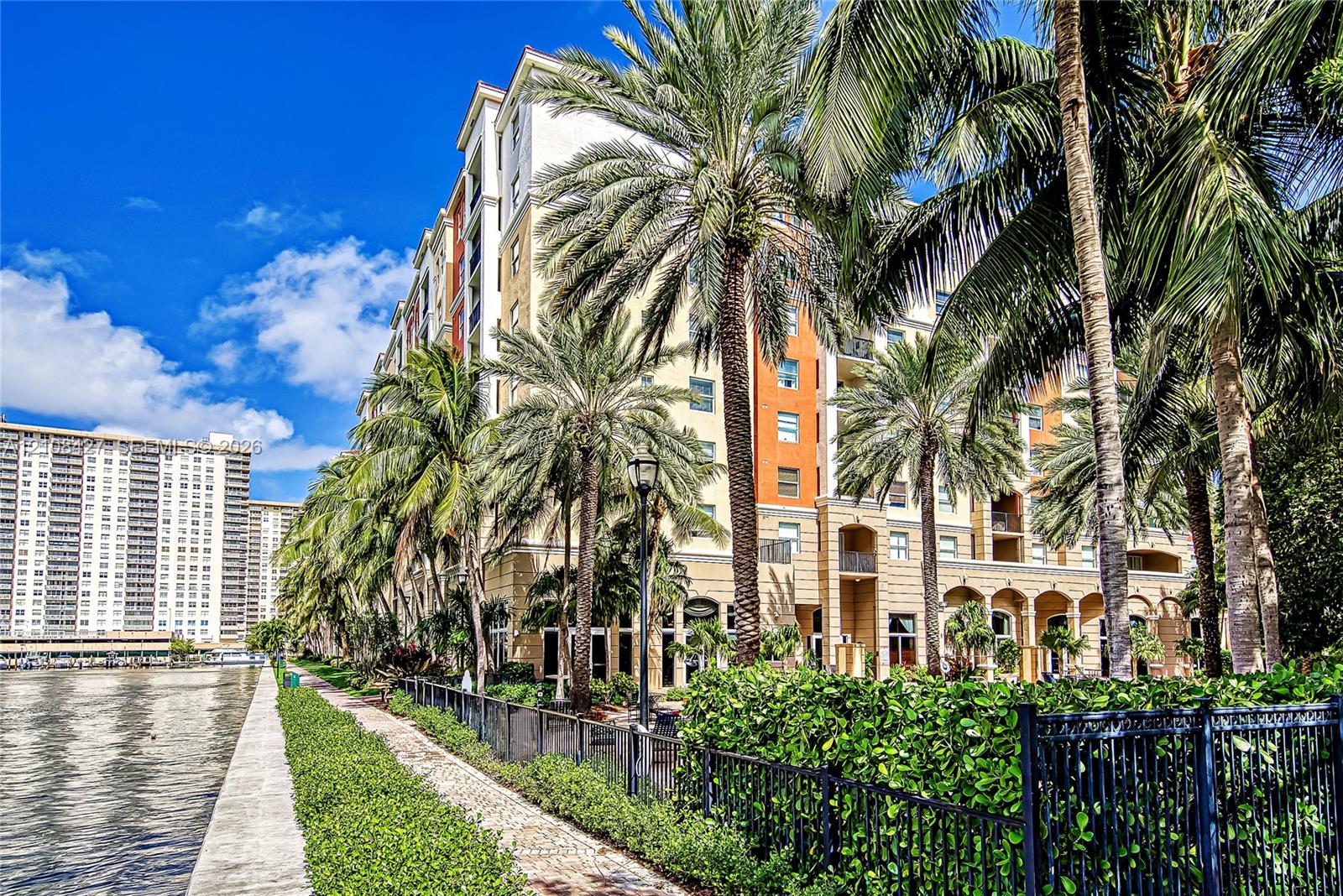 Multi-story exterior featuring a stone-facade, private waterfront promenade, arched architectural detailing, integrated balconies, and mature tropical landscaping