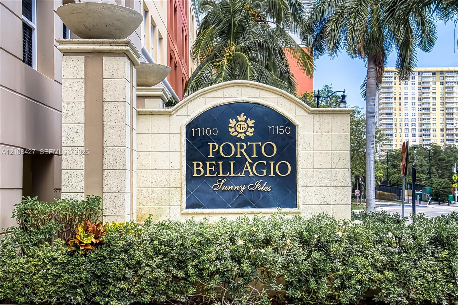Stone-clad monument sign with raised lettering and architectural finials, framed by manicured shrubbery and mature palm trees