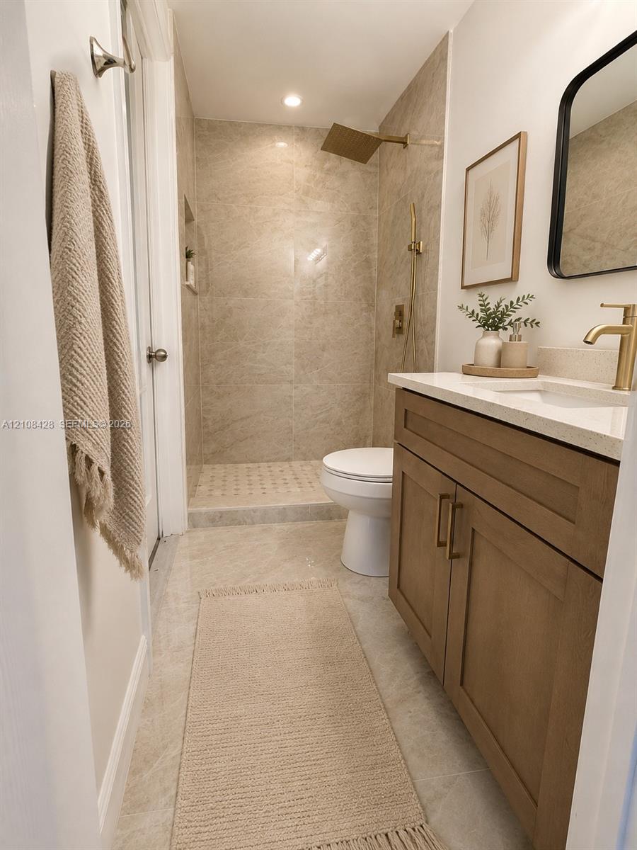 Bathroom featuring a wood-finish vanity with a light-toned countertop, brass-toned hardware, a walk-in shower with stone-style tile, and a rainfall showerhead