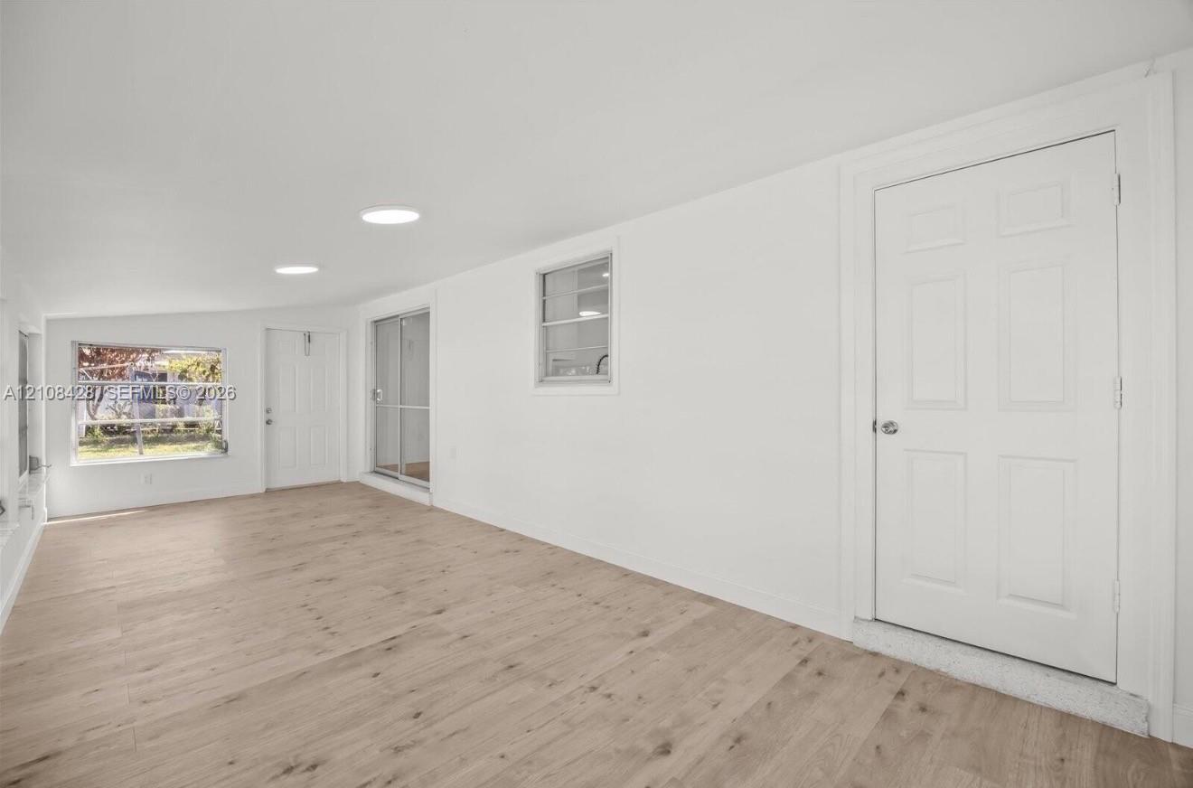 Room featuring wood-finish flooring, two recessed ceiling lights, a glass sliding door, and multiple exterior access doors