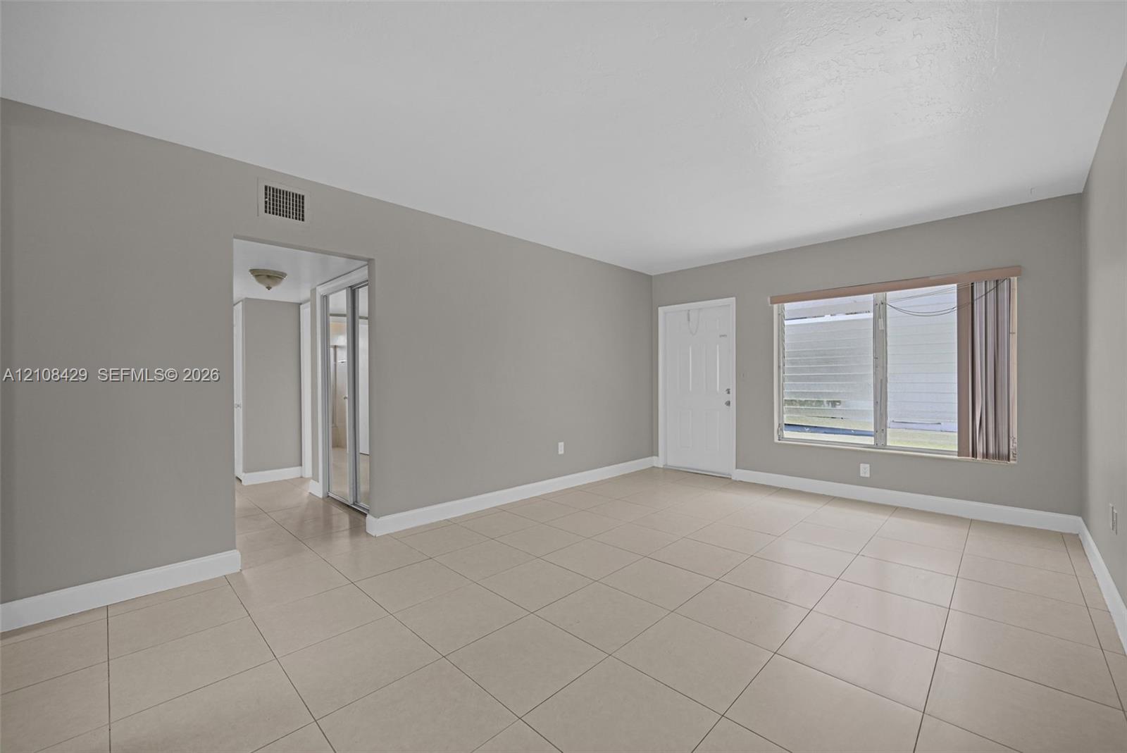 Neutral-toned interior featuring large-format ceramic tile flooring, neutral wall paint, and a wide window with a horizontal blind