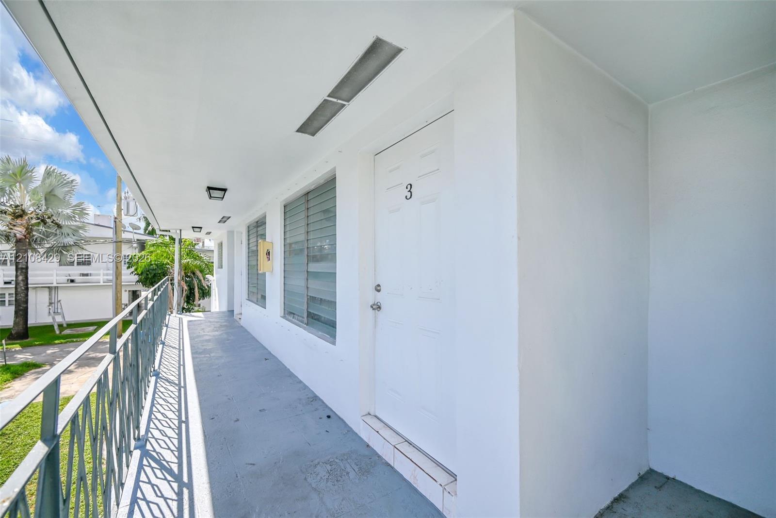 Covered exterior walkway featuring metal railings, horizontal-slatted windows, and recessed ceiling lighting
