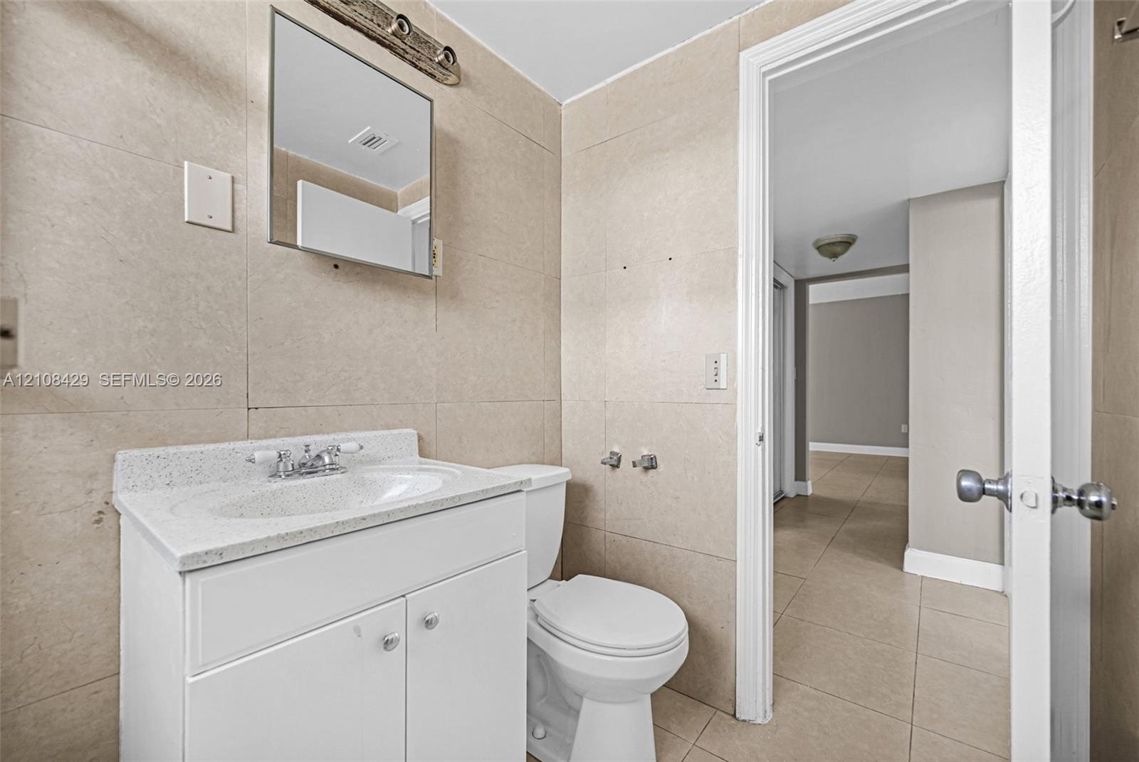 Bathroom featuring large-format wall tiling, white vanity with a solid surface countertop, rectangular under-mount sink, and chrome fixtures