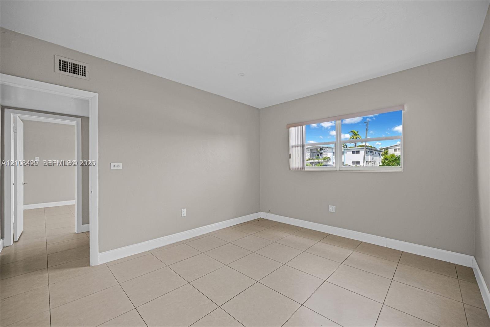Neutral-toned interior space featuring light-colored tile flooring, smooth walls, and a large window with horizontal blinds