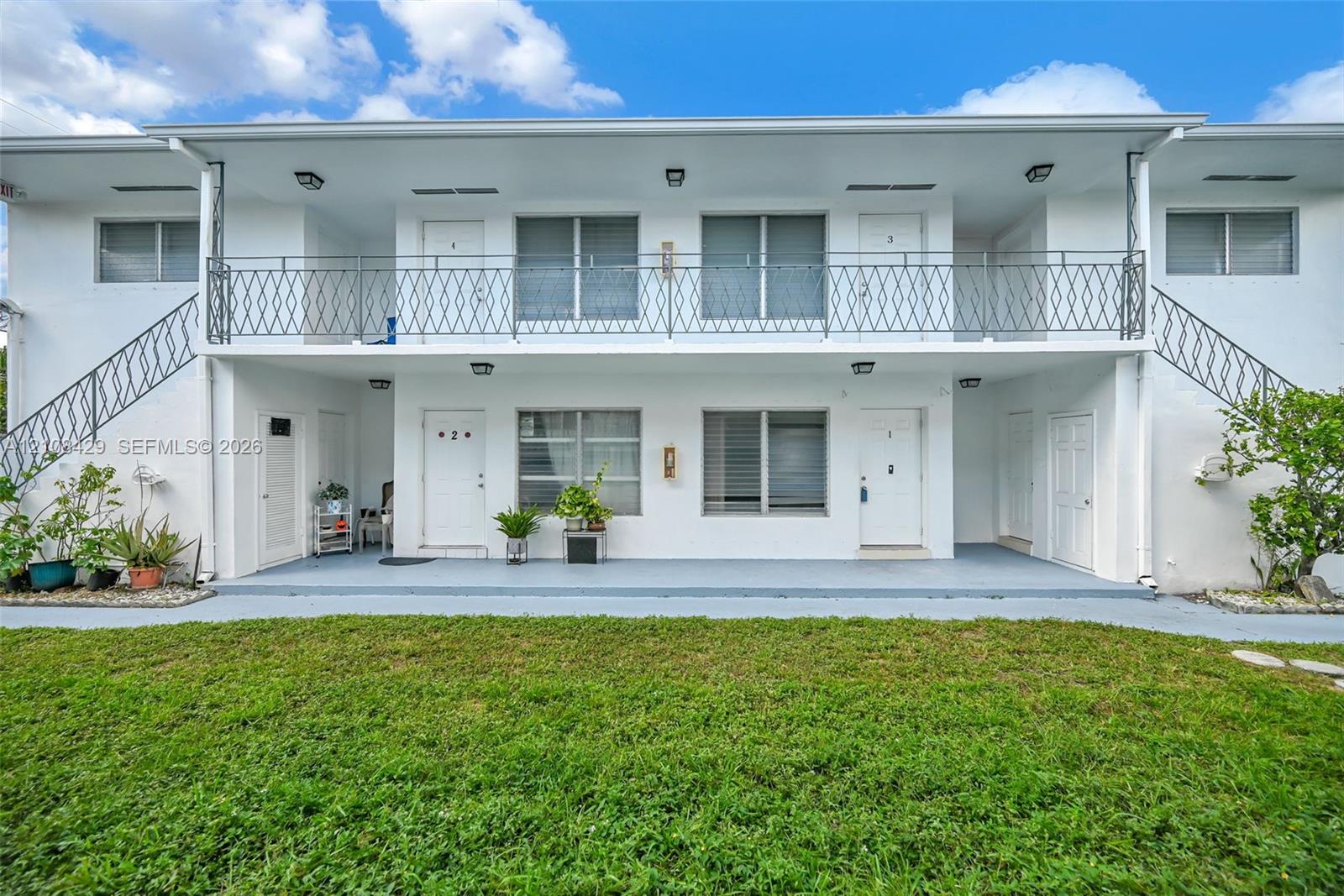 Two-story exterior featuring white stucco siding, dual metal staircases, a second-level metal balcony railing, and concrete ground-level patio space Two-story exterior featuring white stucco siding, dual metal staircases, a second-level metal balcony railing, and concrete ground-level patio space