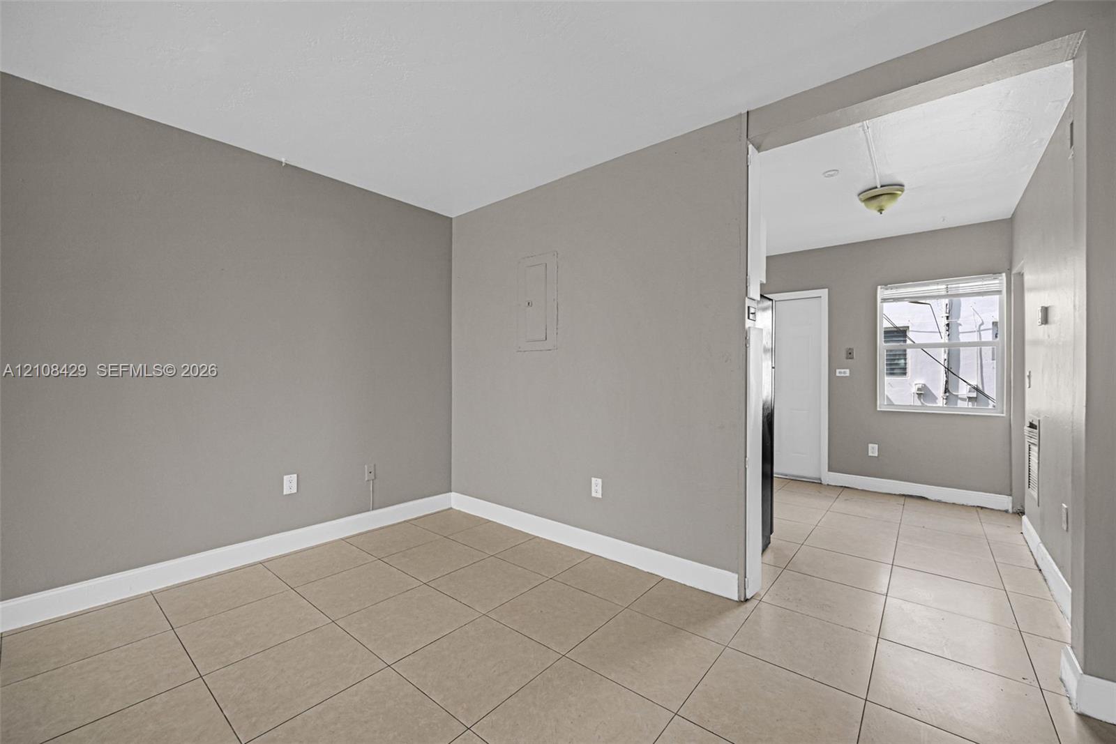 Neutral-toned interior featuring large-format ceramic tile flooring, matte grey wall finishes, and a single-pane window with a horizontal blind