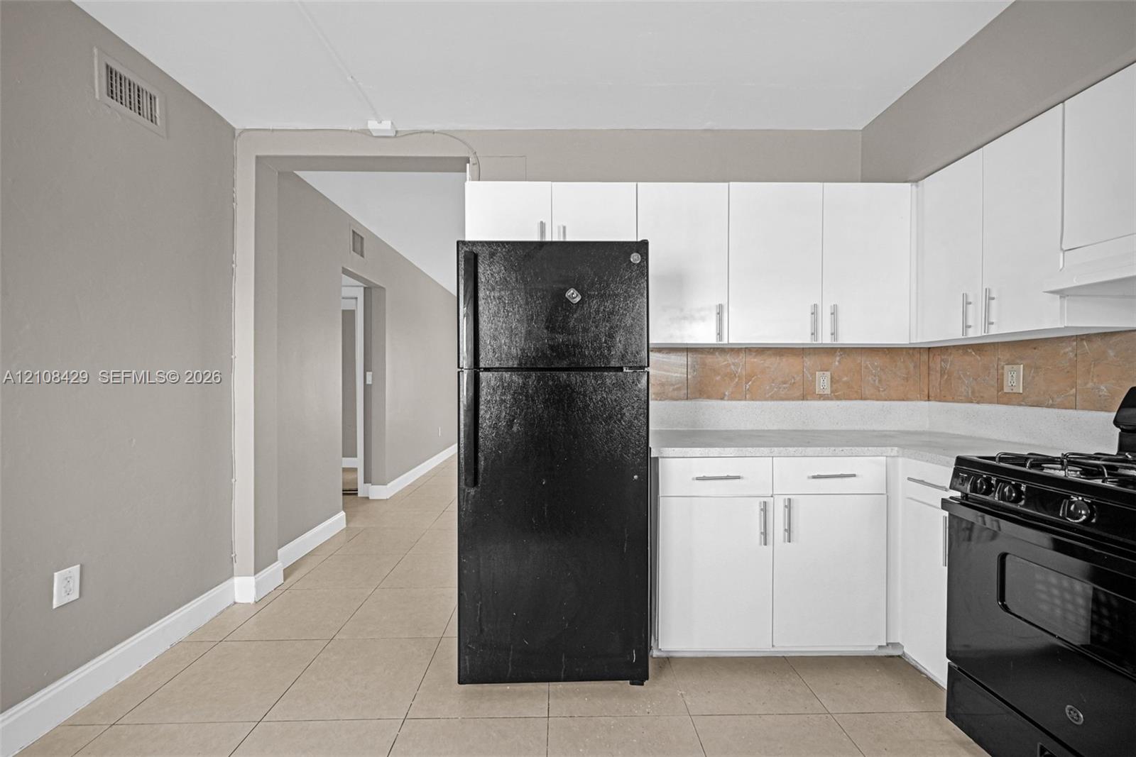 Kitchen featuring white shaker-style cabinetry, matte black appliances, neutral tile flooring, and a stone-tiled backsplash