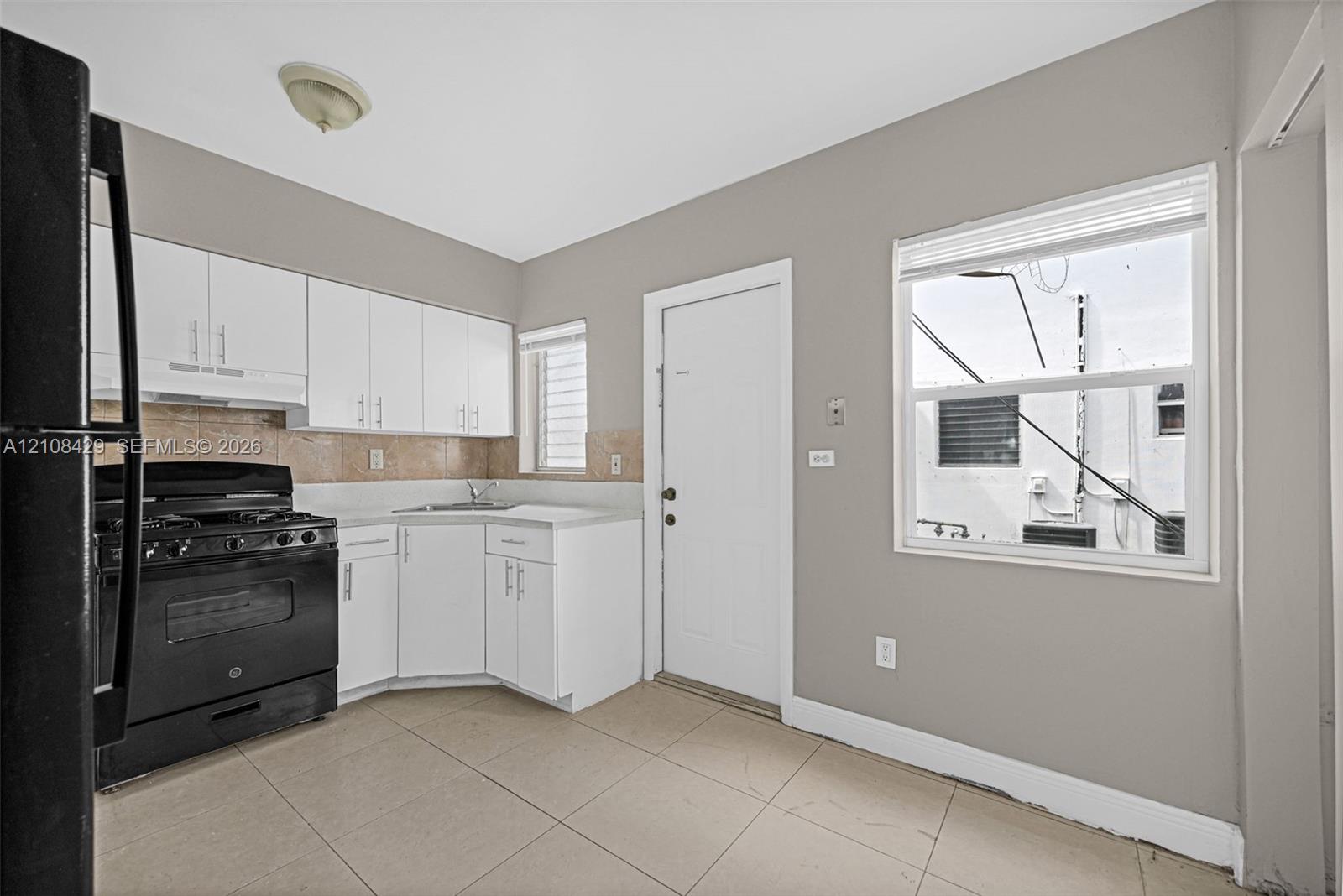 Kitchen featuring white cabinetry, tile flooring, stone-finish backsplash, and black appliances