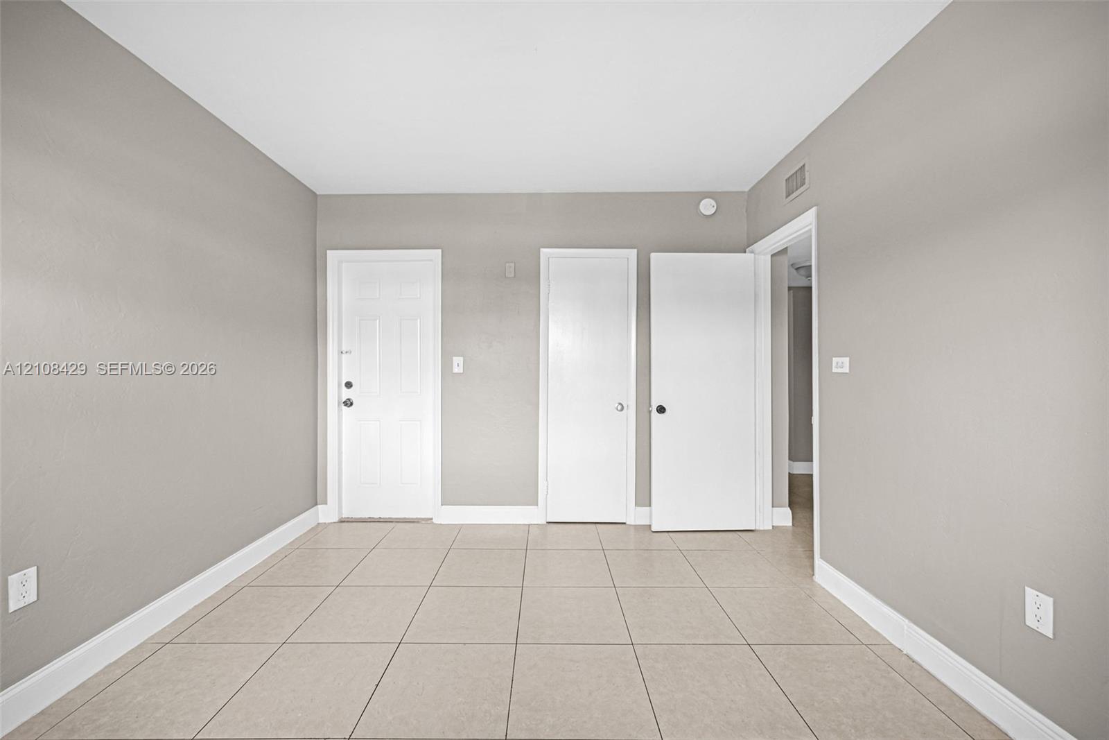 Neutral-toned interior room featuring large-format ceramic tile flooring, three white paneled doors, and smooth, light-grey wall finishes