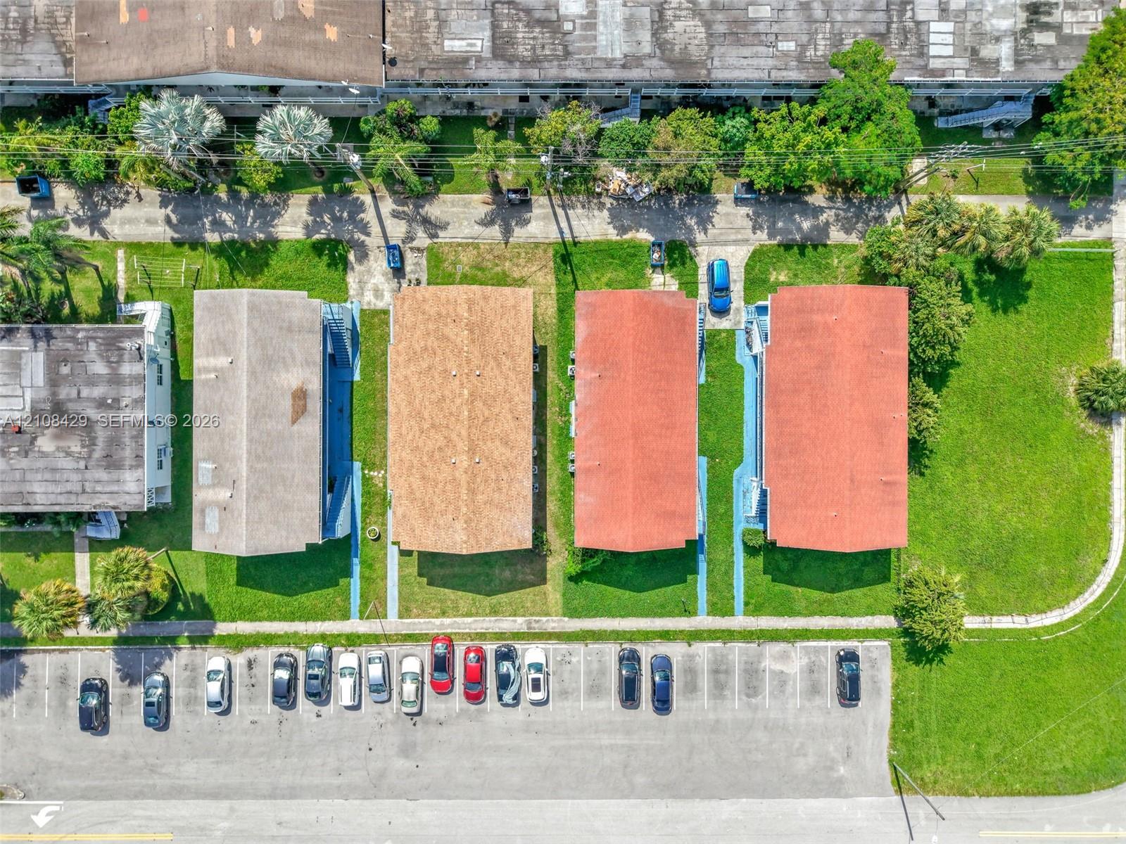 Aerial perspective featuring multiple rectangular residential structures with gabled roofing, integrated walkways, surrounding grass landscaping, and assigned surface parking