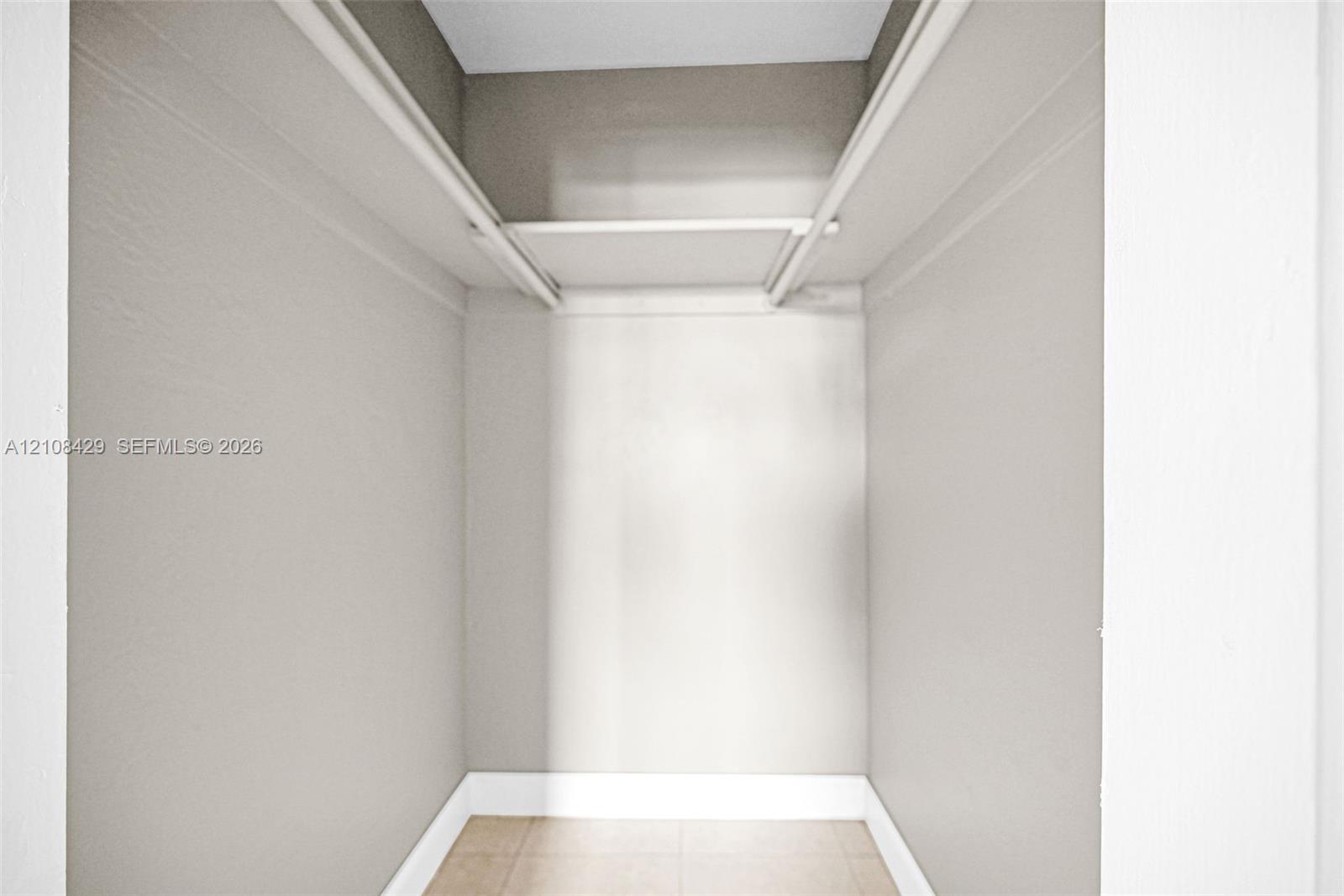 Interior storage space featuring neutral wall paint, a built-in overhead shelf, a hanging rod, and tile flooring