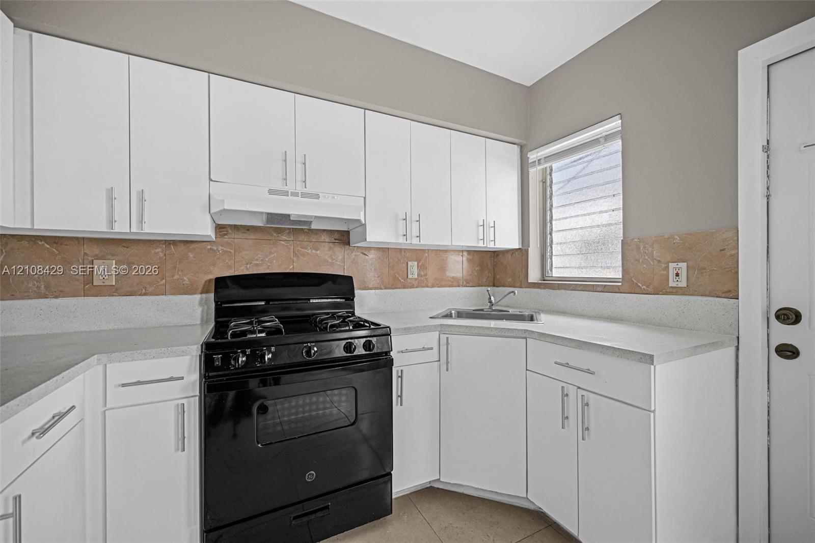 Kitchen featuring white cabinetry, solid-surface countertops, stone-finish backsplash, and a black range