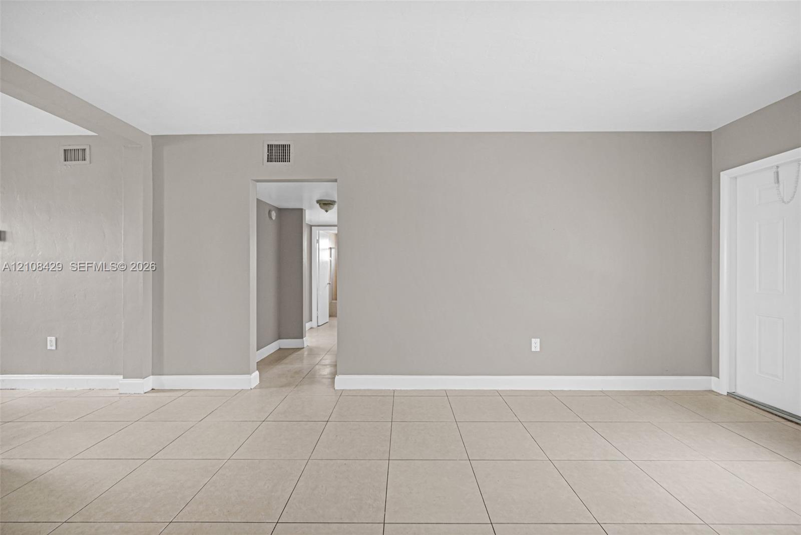 Neutral-toned interior space featuring large-format ceramic tile flooring, solid-core interior doors, and a recessed doorway leading to an additional interior space