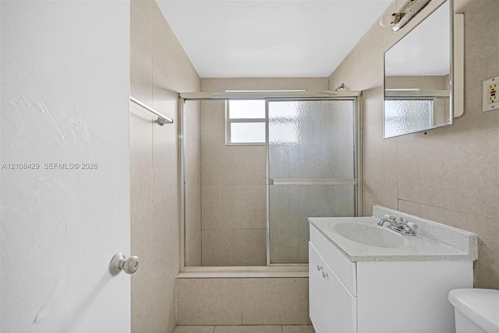 Bathroom featuring a shower-tub combination with sliding glass doors, neutral tile wall surround, white vanity with a composite countertop, and an integrated mirrored medicine cabinet