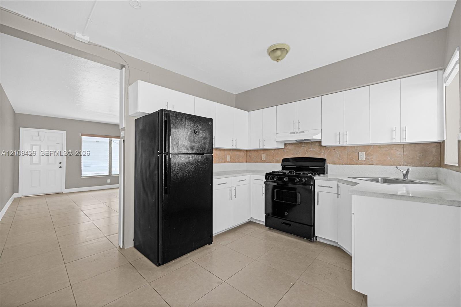 Kitchen featuring white cabinetry, solid-surface countertops, stone-finish backsplash, and black appliances