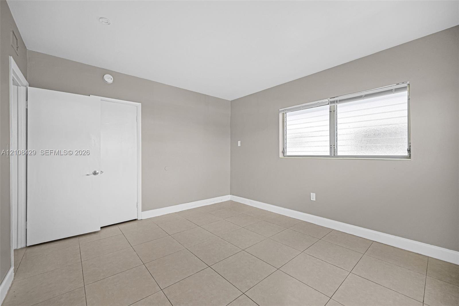 Neutral-toned interior space featuring large-format ceramic floor tiles, recessed ceiling lighting, and a dual-panel door