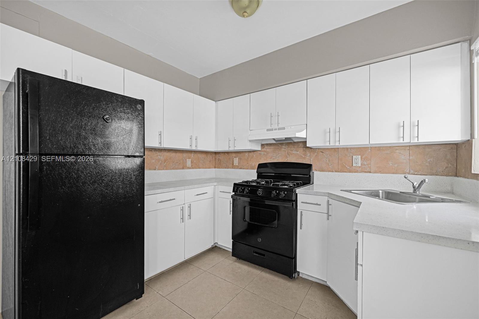 Kitchen featuring white shaker-style cabinetry, solid-surface countertops, tile backsplash, tile flooring, and black appliance suite