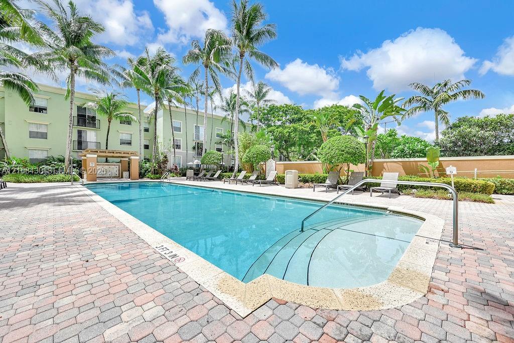 Swimming pool with stepped entry, surrounding brick paver deck, and lush tropical landscaping