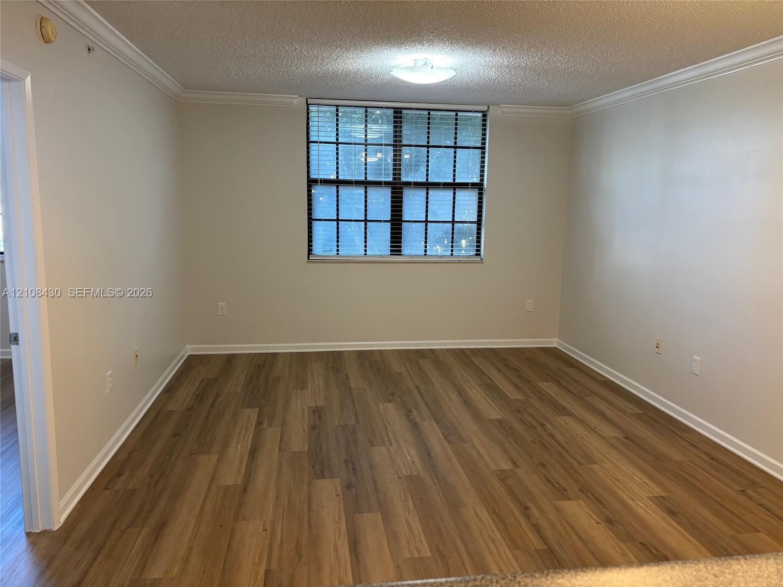 Room interior featuring wood-finish flooring, neutral wall tones, multi-pane window with horizontal blinds, and crown molding