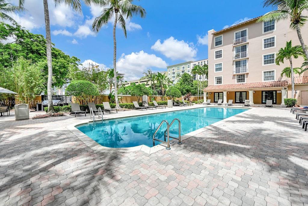 In-ground swimming pool with a stone paver deck, perimeter landscaping, and mature palm trees