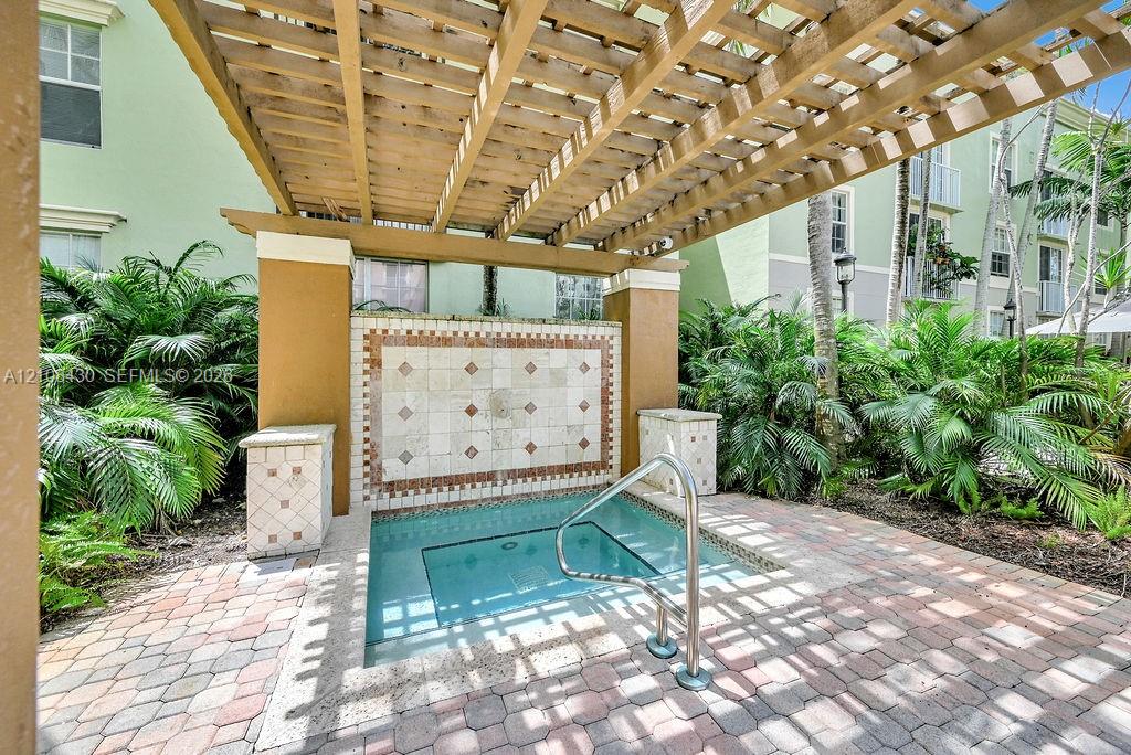 Outdoor spa featuring a concrete paver deck, a wood-beam pergola, decorative tile masonry, and integrated metal handrail