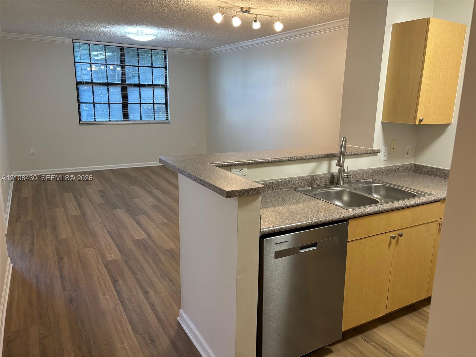 Kitchen featuring light wood-finish cabinetry, solid-surface countertops, dual-basin stainless steel sink, stainless steel dishwasher, and wood-finish flooring
