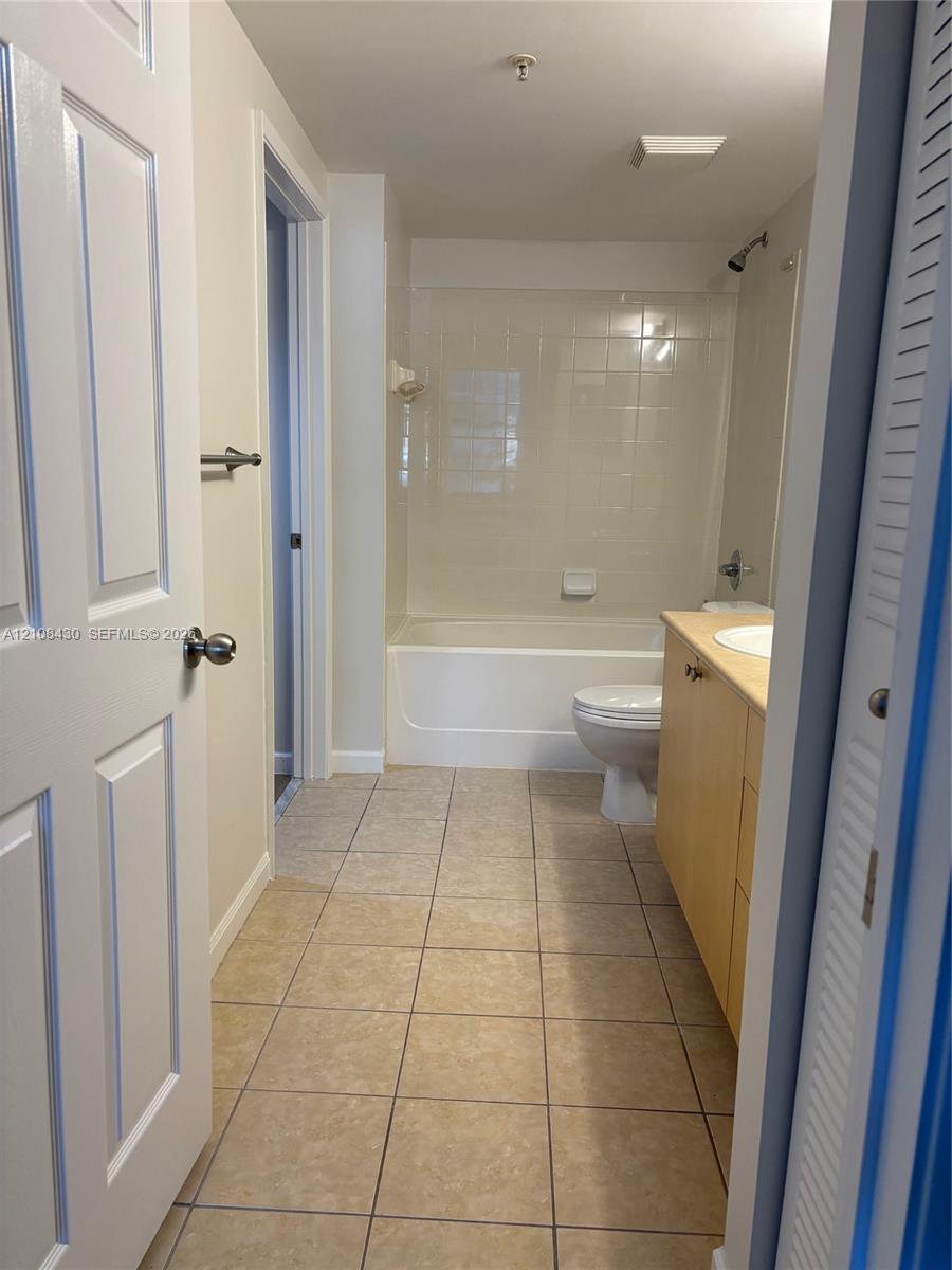 Bathroom featuring tile flooring, a tub-shower combination with full-height tile surround, and a wood-finish vanity cabinet with a drop-in sink