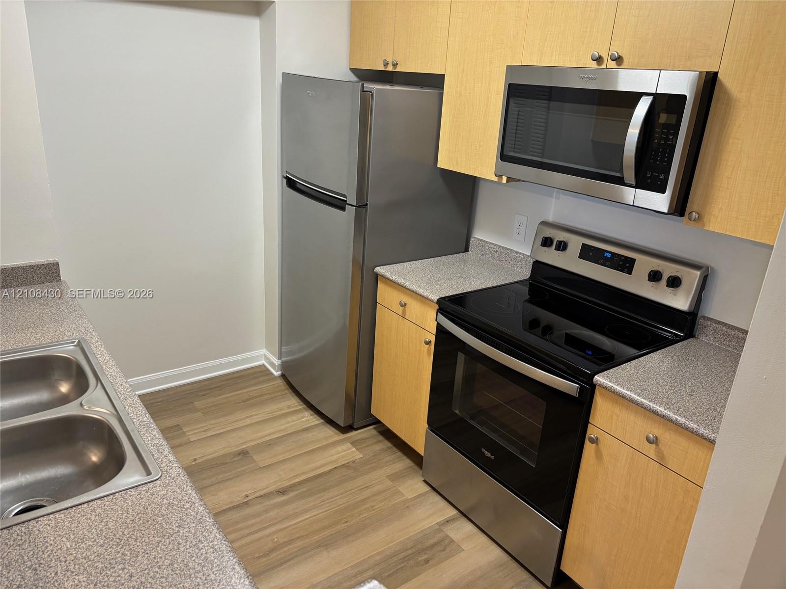 Kitchen featuring wood-finish cabinetry, stone-texture countertops, stainless steel appliances, and wood-finish flooring