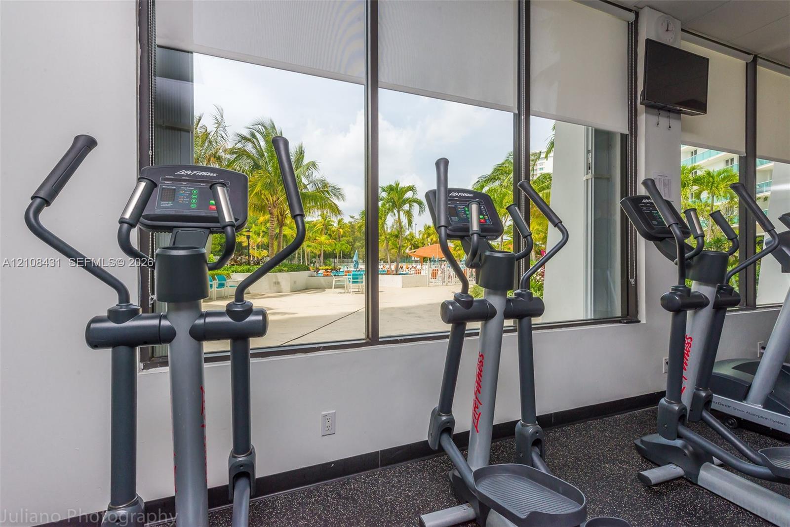 Fitness center featuring floor-to-ceiling windows, retractable solar shades, and industrial rubber flooring