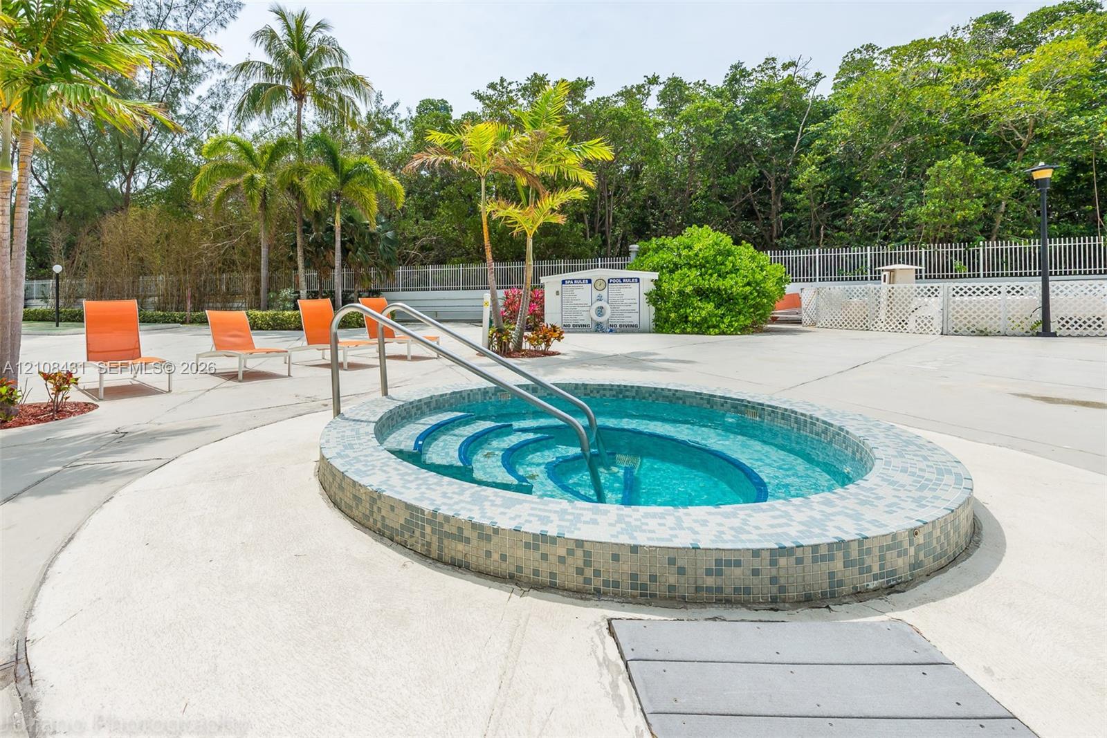 Circular jetted spa featuring a tile-accented exterior, built-in entry steps, stainless steel handrail, and a surrounding concrete deck