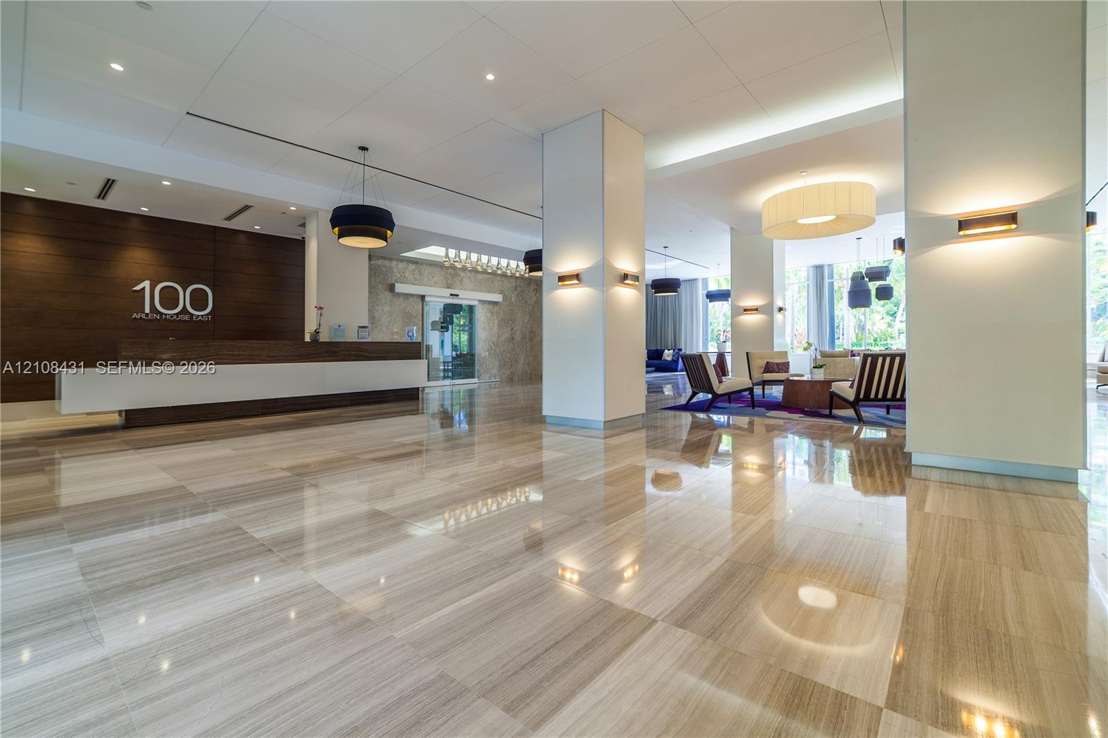Expansive lobby featuring polished stone flooring, wood-paneled reception desk, structured support columns, and layered architectural lighting Expansive lobby featuring polished stone flooring, wood-paneled reception desk, structured support columns, and layered architectural lighting