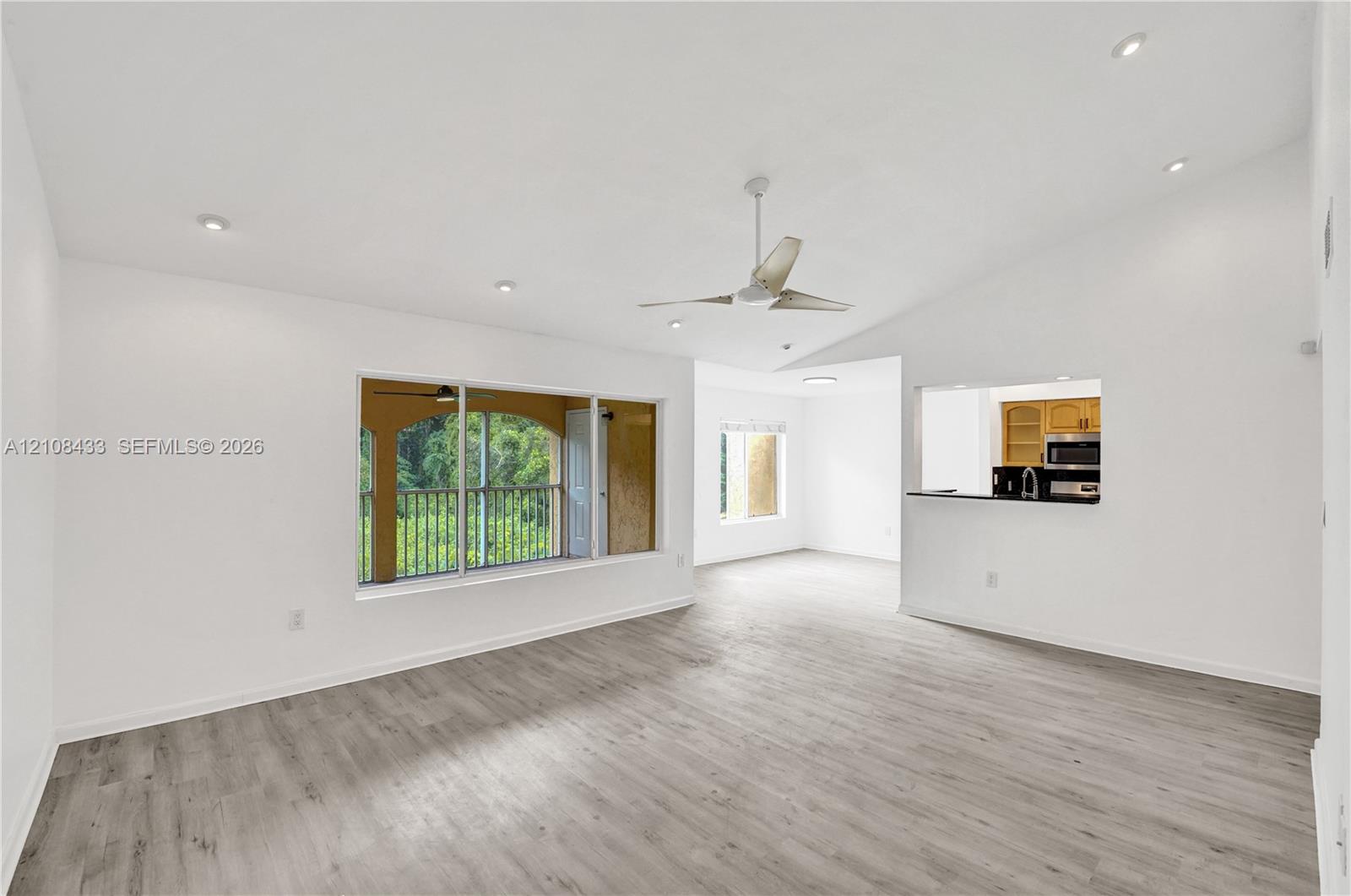 Open living area featuring vaulted ceilings, wood-finish flooring, recessed lighting, a ceiling fan, and a pass-through opening to the kitchen