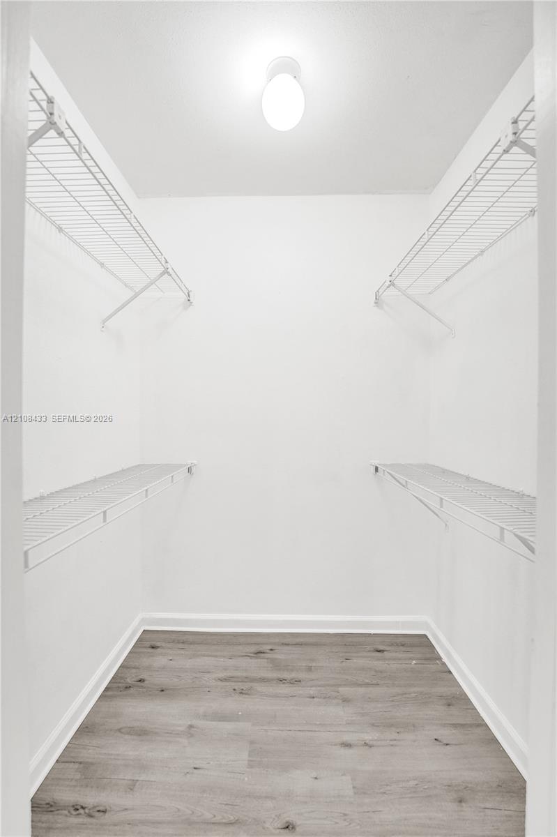 Walk-in closet featuring dual-level white wire shelving, flush-mount dome lighting, and wood-finish flooring