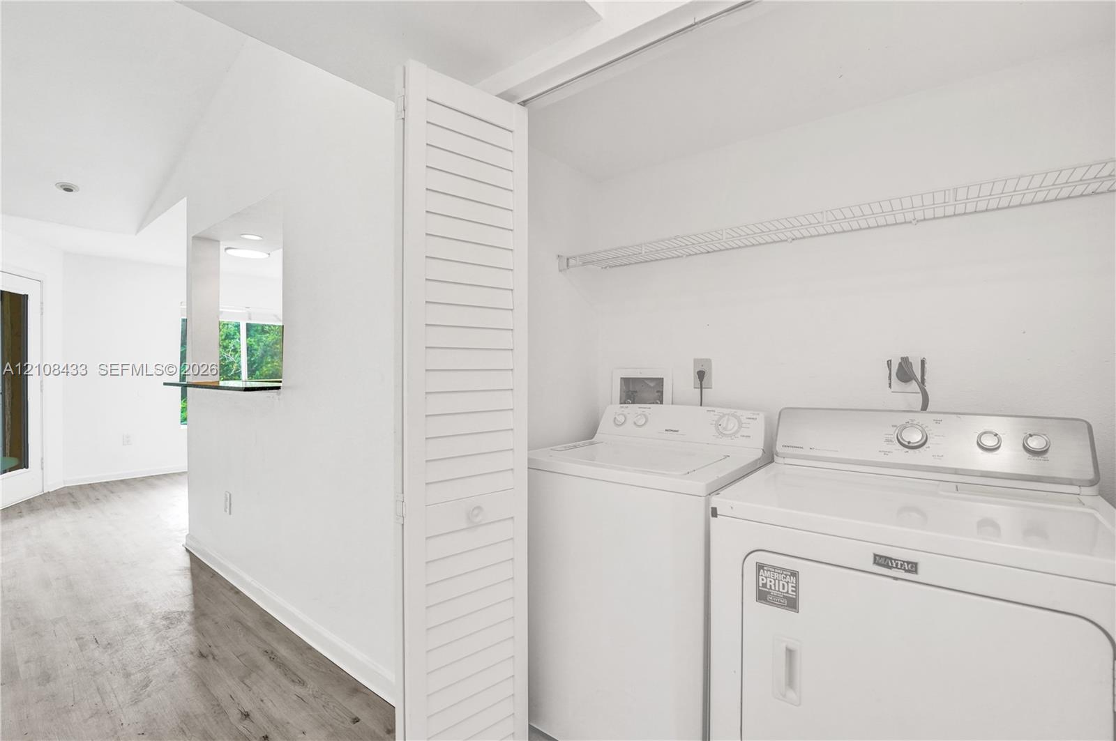Laundry closet featuring louvered bi-fold doors, overhead wire shelving, and wood-finish flooring